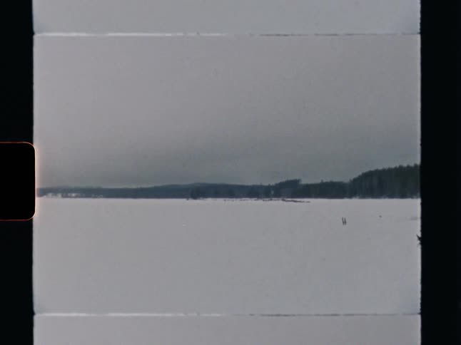 Vintage 8mm film captures a desolate view of a snow-covered frozen lake in winter