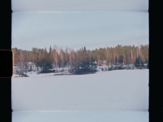 A vintage Super 8 film captures a tranquil winter scene of a snow-covered, frozen lake and a distant forest