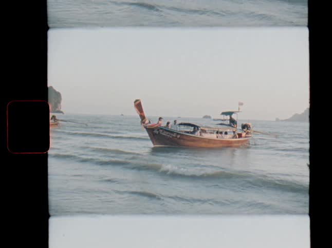 A vintage film shot shows a traditional Thai longtail boat rocking gently on the calm ocean waves