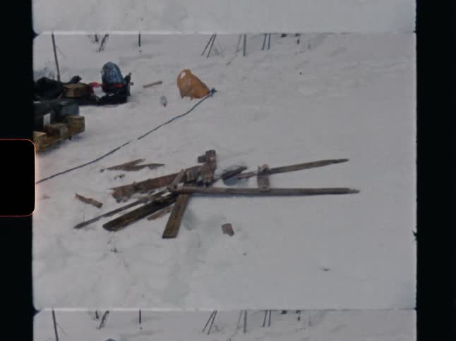 Vintage 8mm film shows a messy winter campsite with a broken wooden sled in the snow