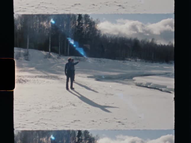 A retro Super 8 film captures two people exploring a sunny, snowy landscape beside a frozen river