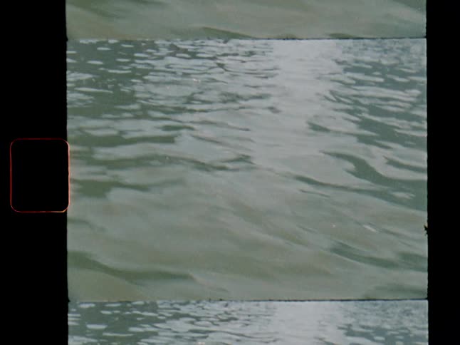 Vintage film captures sunlight reflecting on gentle river waves, revealing people in canoes in the background