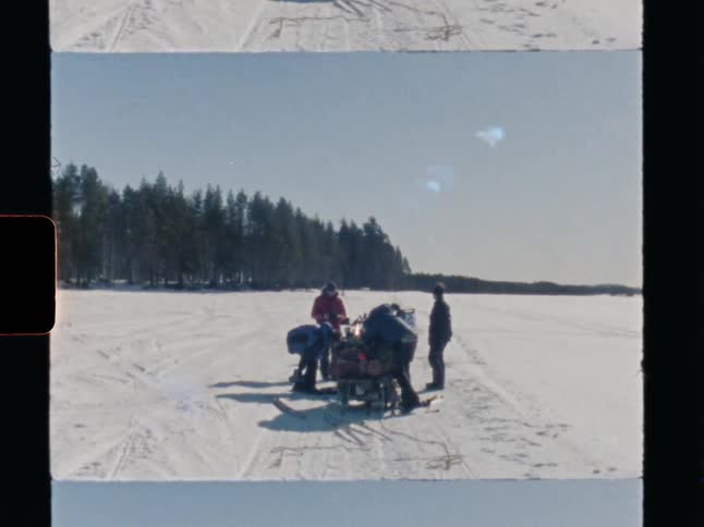 Vintage 8mm film captures a group of adventurers taking a break on a vast snowy landscape with their gear-laden sled