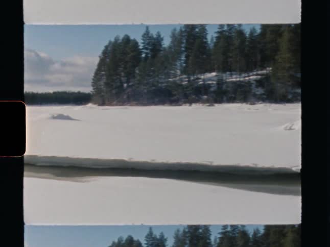 A scenic pan across a snow-covered frozen lake in winter, revealing a dense pine forest on a partly cloudy day