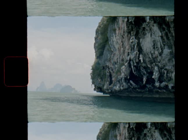 A scenic, vintage film-style shot captures a majestic limestone cliff rising from the calm sea, with hazy islands in the distance