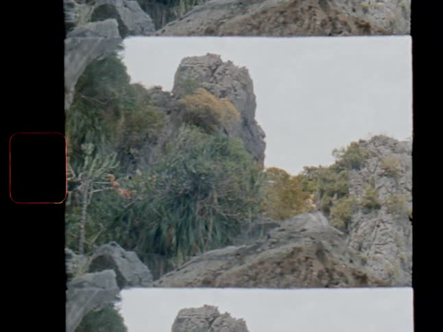 A vintage film pan across a rugged, tropical, rocky hillside covered in lush green vegetation, framed with a split screen effect