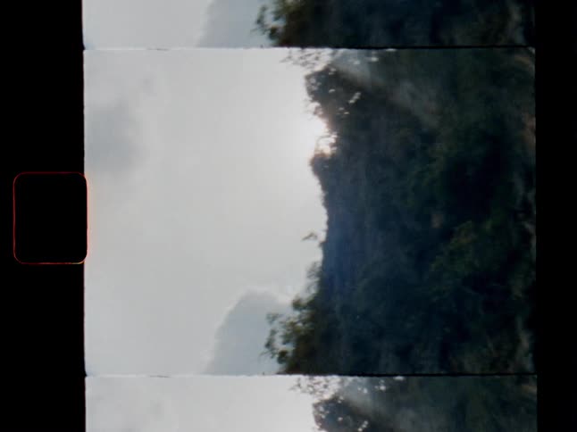 A vertical 8mm film scan captures the sun emerging from behind a tree-covered mountain, with beautiful sunbeams breaking through the clouds
