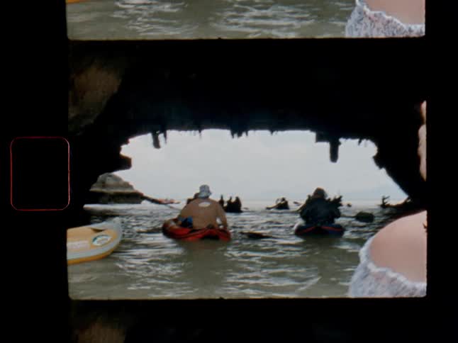 A scanned film strip captures a group of tourists in kayaks paddling out of a dark, rocky sea cave