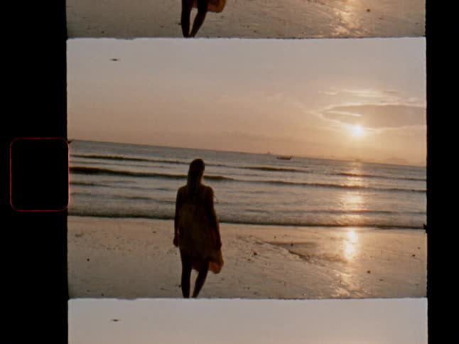 Vintage film footage captures a woman in a yellow dress walking barefoot along the shoreline towards the setting sun