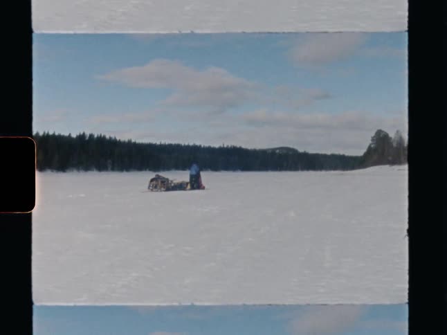 Vintage 8mm footage captures a solitary figure with a snowmobile on a vast, frozen lake in a remote winter landscape