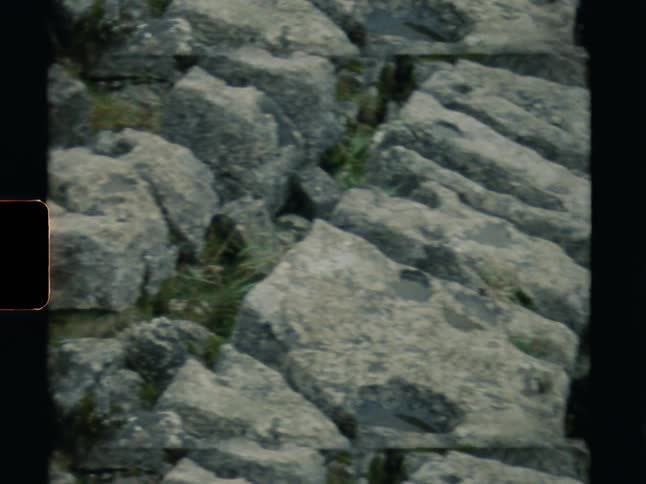 An abstract top-down view slowly pans across ancient, weathered rock formations on vintage film