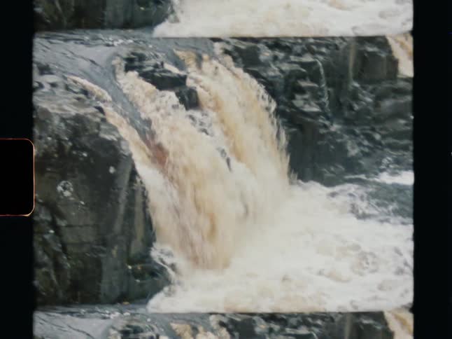 A scenic pan across a rushing river and small waterfall captured on vintage Super 8 film