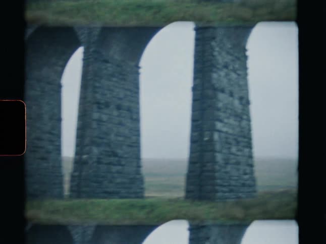 An authentic Super 8 film scan reveals a slow pan across the arches of a majestic stone viaduct in the misty, green countryside