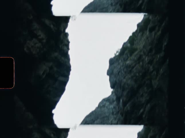Vintage 8mm film captures a tilt-down shot of a waterfall cascading through a rocky gorge