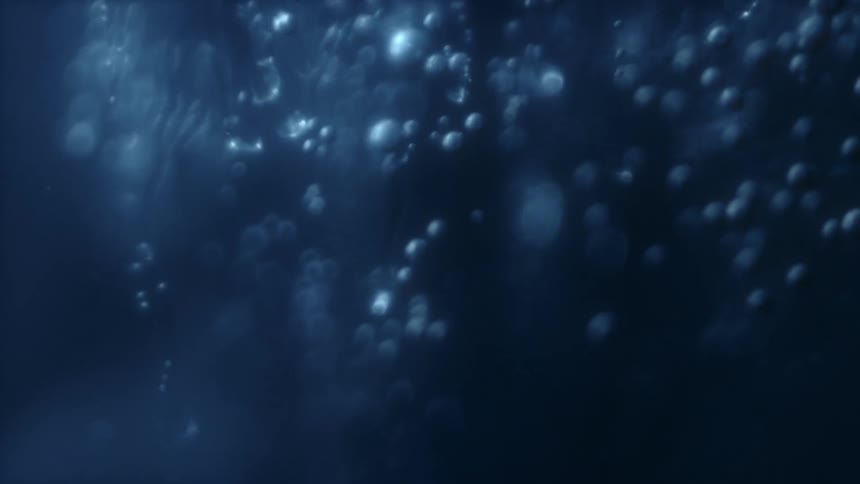 Bokeh bubbles float gently upwards through mysterious, deep blue water