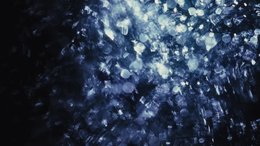 Abstract ethereal blue light particles shimmer and sparkle against a dark, mysterious background