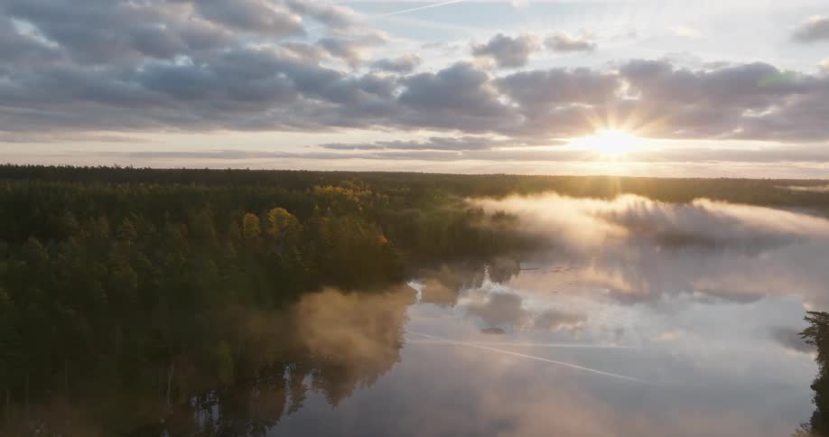 A tranquil aerial shot reveals a stunning sunrise over a misty lake and expansive autumnal forest