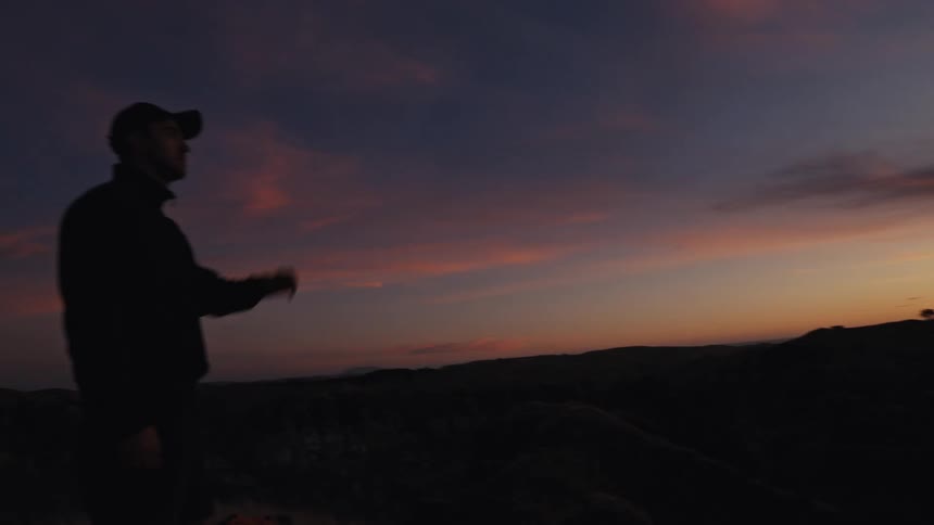 A man's silhouette is revealed as he takes off his cap to watch a beautiful sunset from a hilltop