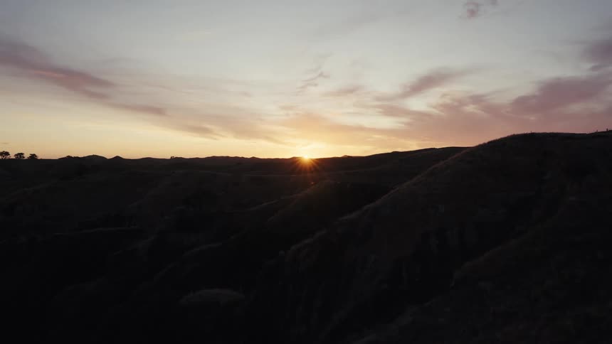 A static shot of a golden sun setting behind the dark, rolling hills under a colorful sky
