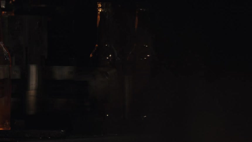 Abstract close-up of empty glass bottles moving on a conveyor belt in a dimly lit manufacturing plant