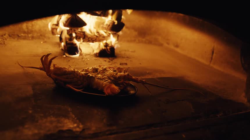 A delicious lobster is cooked in a traditional wood-fired oven with flames in the background