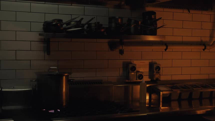 A large stainless steel pot steams on a gas stove in a dark, atmospheric restaurant kitchen