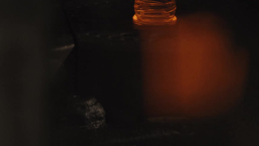 A close-up view of a machine crafting glowing hot glass into bottle tops in a dark factory setting