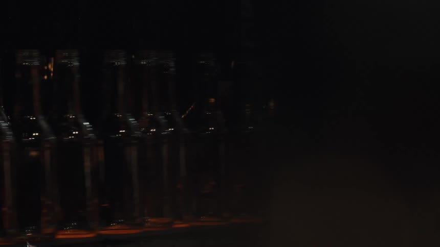 An industrial conveyor belt transports newly formed glass bottles in a dimly lit factory