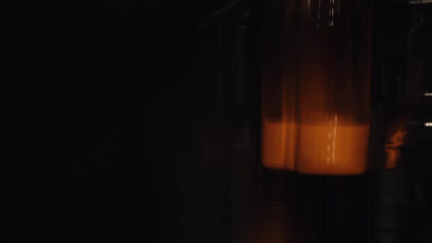 A close-up view shows glowing hot glass bottles moving along a factory production line after being molded