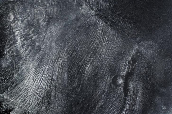 A macro view of a dark, shimmering metallic liquid slowly flowing and creating abstract textures