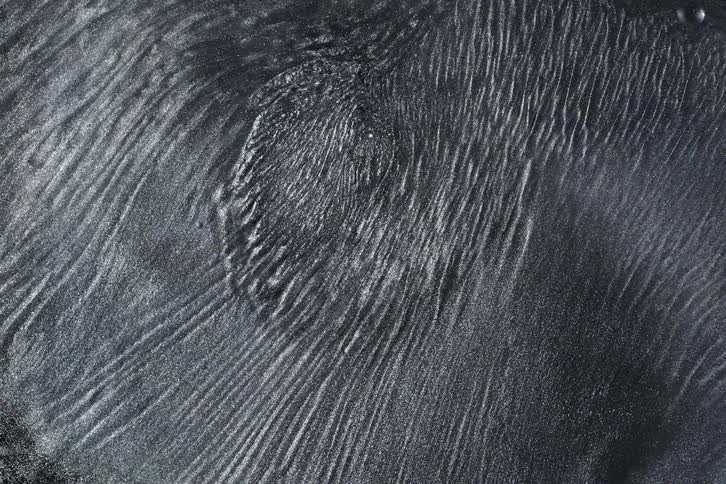 Hypnotic patterns form on the surface of a dark, viscous, metallic liquid, reacting to an unseen magnetic force