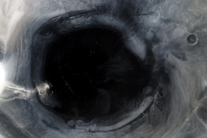 Ethereal white and silver smoke slowly swirls and expands into a dark void, creating a cosmic and mesmerizing abstract background
