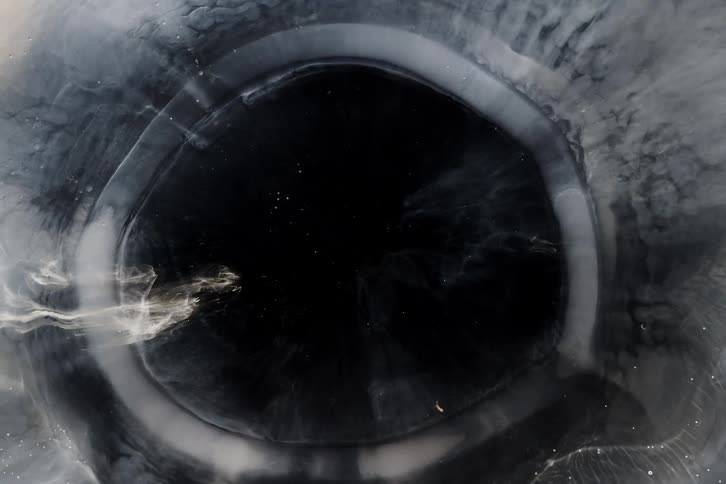 A mesmerizing macro shot of dark, veiny ink slowly expanding and opening into a deep black void
