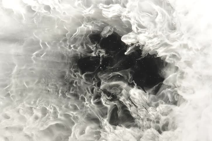 Ethereal white ink billows and swirls in water, creating a mesmerizing abstract celestial pattern around a dark void