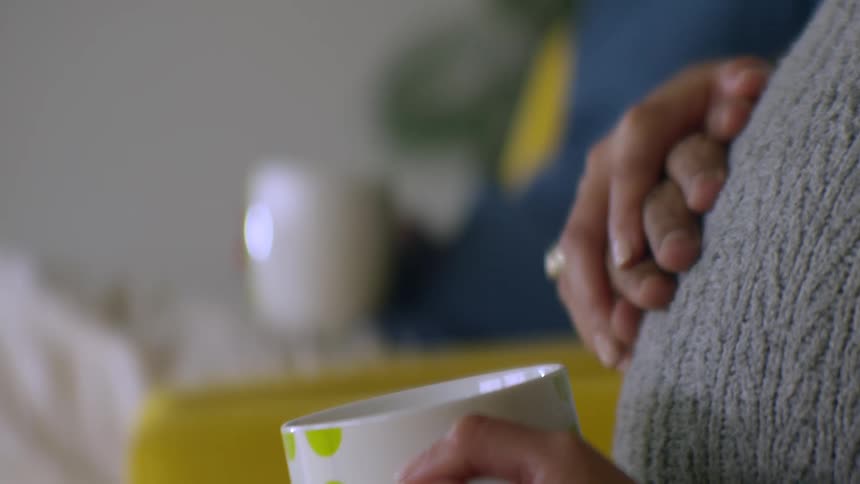 An intimate slow-motion rack focus from an expecting couple holding hands on the baby bump to the loving face of the father-to-be