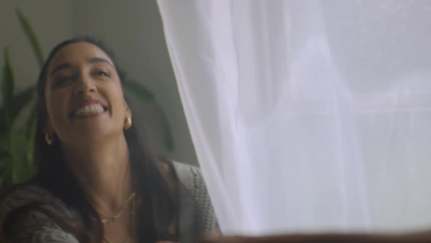 A man reaches for his partner's hand through a sheer white curtain, then gently caresses her face in a romantic slow-motion close-up