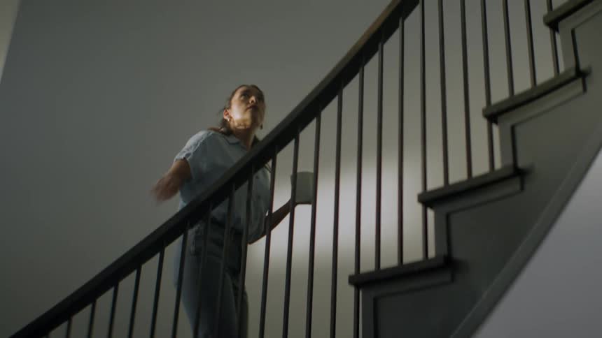 A woman carrying a coffee mug slowly and cautiously walks up a modern staircase in her home