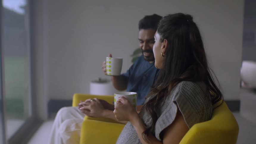 A loving expectant couple share a peaceful moment at home, drinking from mugs and enjoying each other's company in their modern living room