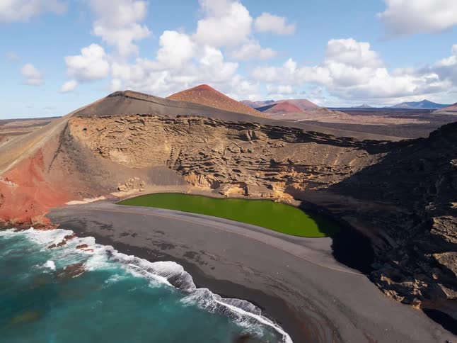 Aerial pullback reveals the stunning Charco de los Clicos, a vibrant green lagoon on a black volcanic beach in Lanzarote, Spain