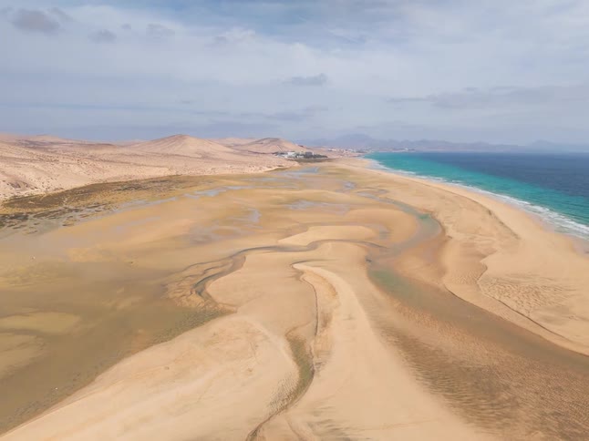 An epic aerial drone shot pulls back to reveal a stunning and vast desert coastline where intricate tidal flats meet the turquoise sea
