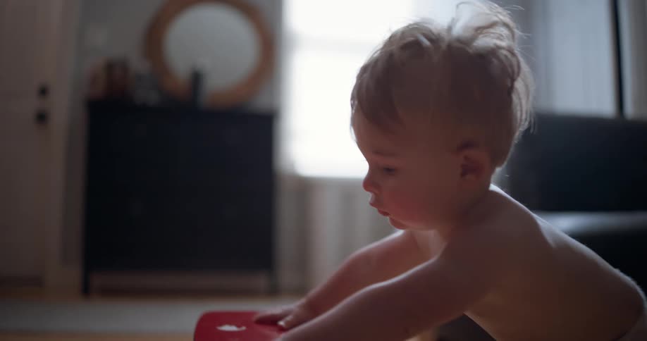 Cute baby boy in a diaper learns to walk by pushing a colorful toy piano across the floor in slow motion