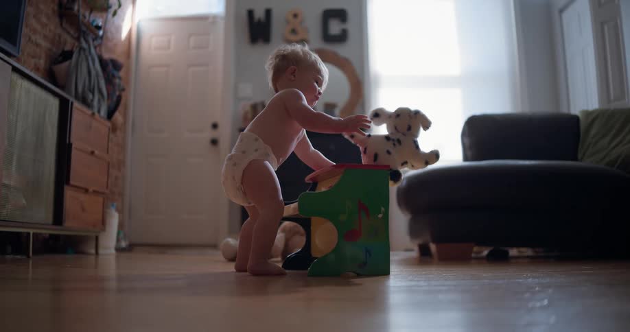 A baby in a diaper playing with a toy piano pushes a stuffed dog off in slow motion