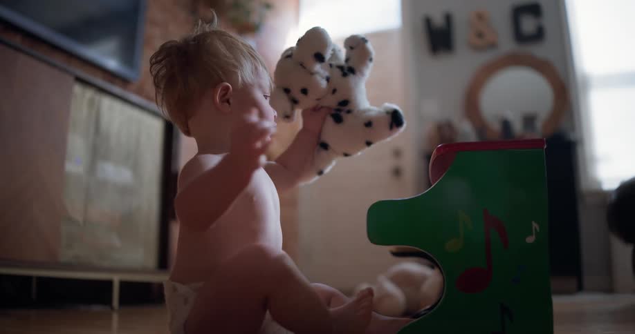 An adorable baby boy sits on the floor in slow motion, playing intently with his stuffed dog and a small toy piano