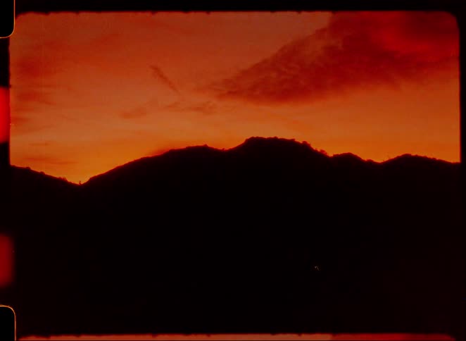 A fiery red and orange sunset behind a mountain silhouette captured on vintage film with intense light leaks and scratches