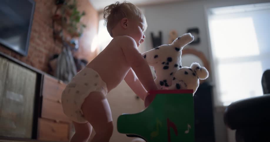 A baby in a diaper pulls himself up on a toy piano and plays with his stuffed dalmatian in slow motion