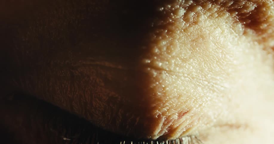 The eyelid of a human with a detailed blue iris closes slowly in a dramatic macro shot