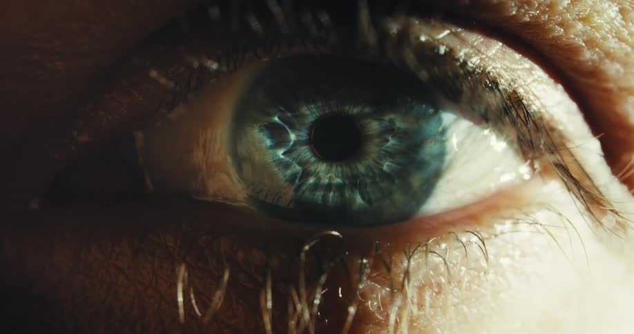 A dramatic macro shot captures a wet, blue eye opening slowly as a single tear clings to the lower lashes