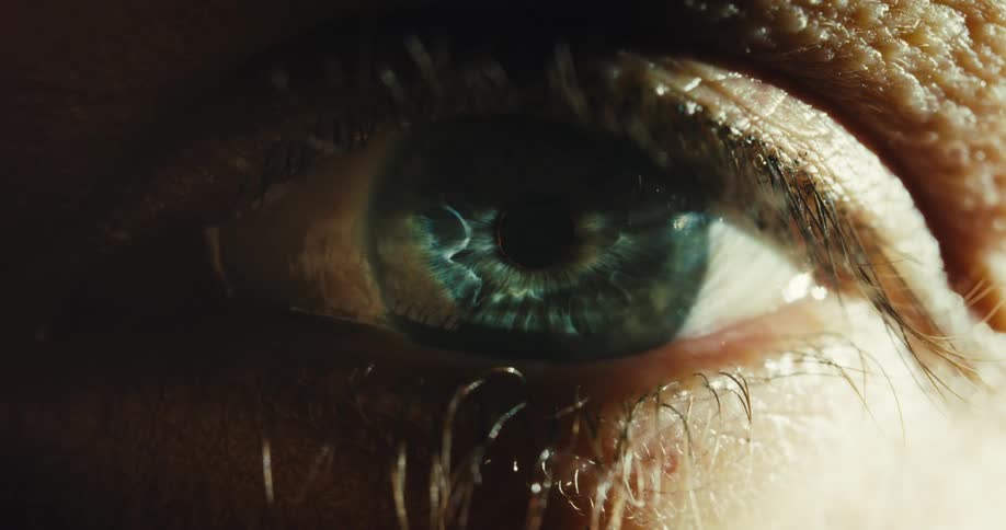 A dramatic extreme close-up of a human eye slowly opening, revealing a detailed blue iris