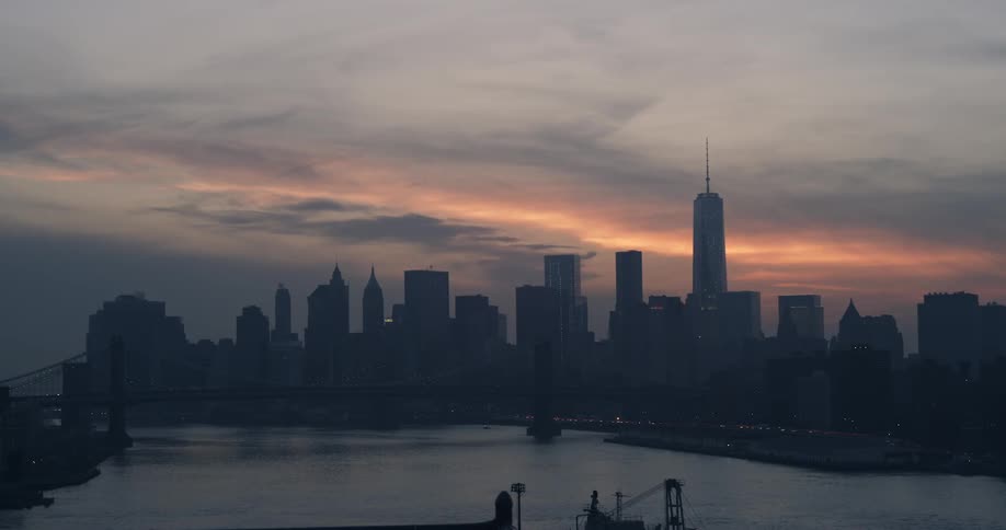 View of a bridge, city skyline and a body of water during sunset on a cloudy evening