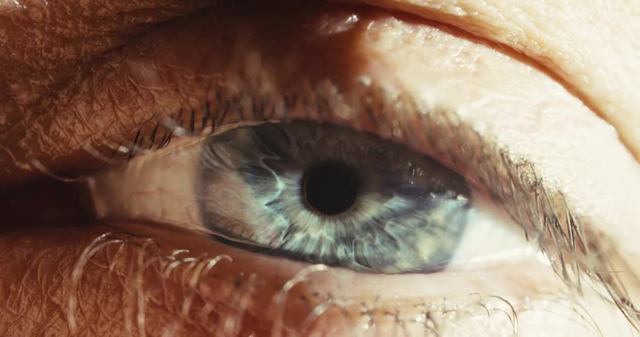 An intense macro shot reveals the intricate details of a beautiful blue human eye as it slowly turns to look into the camera